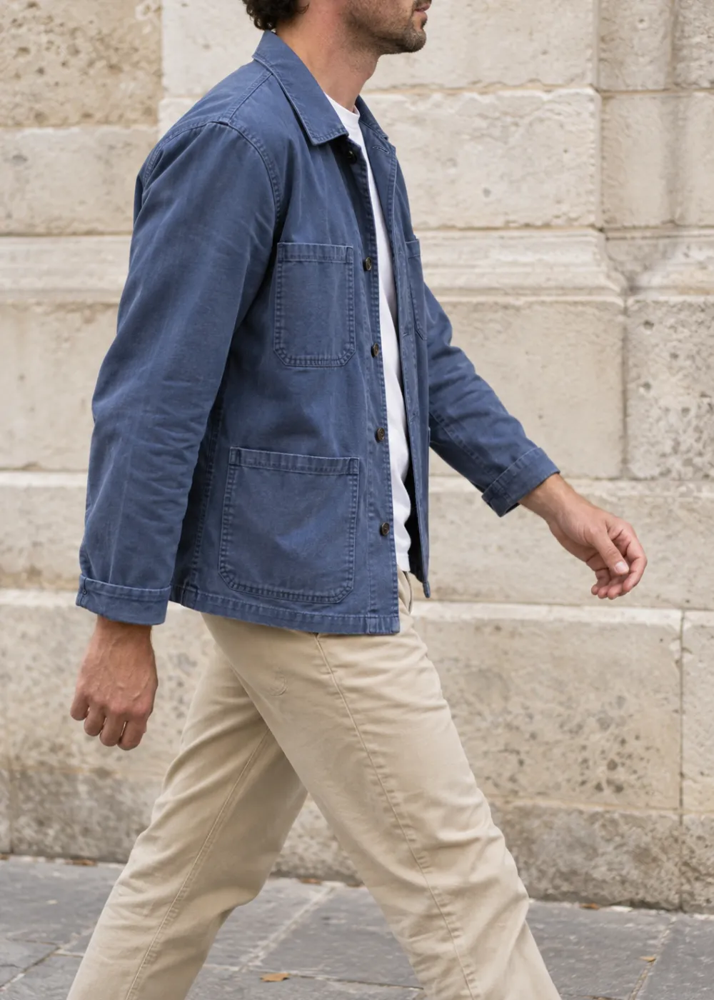 Hombre caminando de perfil con chaqueta de trabajo azul de algodón y chino beige