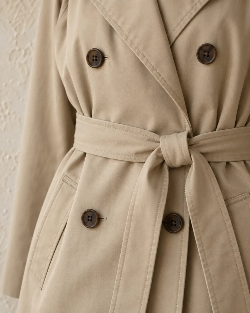 Detalle del cinturón anudado y los botones de la gabardina beige de algodón